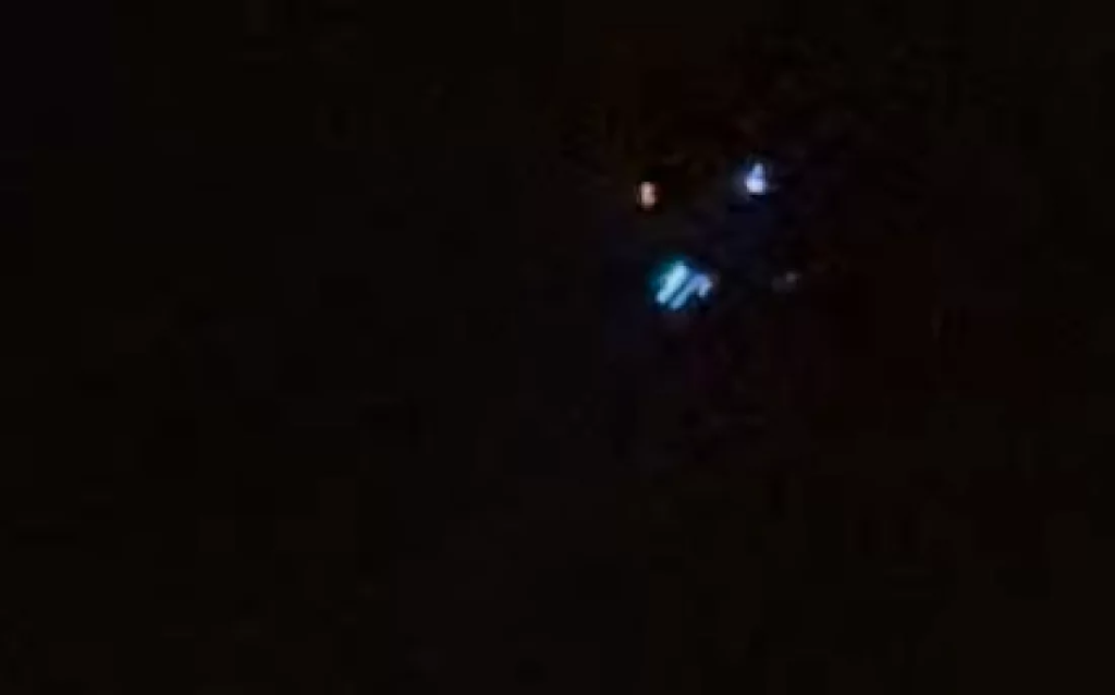 Large drones flying in formation over a suburban New Jersey neighborhood during the night, emitting bright lights against a dark sky.